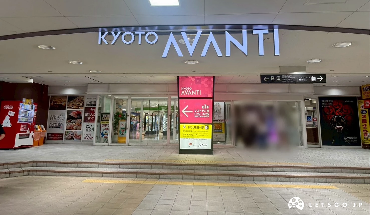 B1「KYOTO AVANTI」亮藍色霓虹燈品牌招牌與商場大門入口的夜間街景。