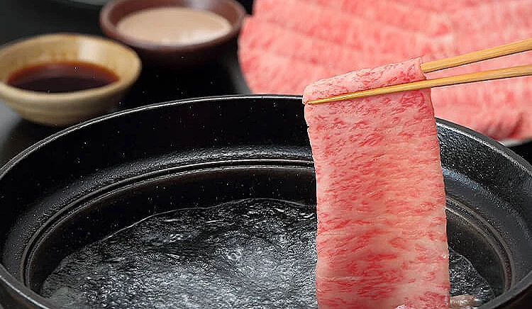 用筷子夾起的霜降和牛涮肉片與沾醬