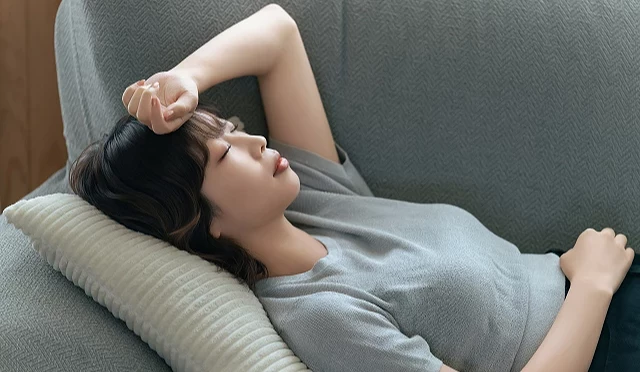 疲憊女性躺在沙發上閉眼休息,手臂覆在額頭上
