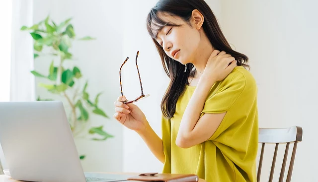 女性坐在筆電前取下眼鏡,閉眼按壓肩頸部位