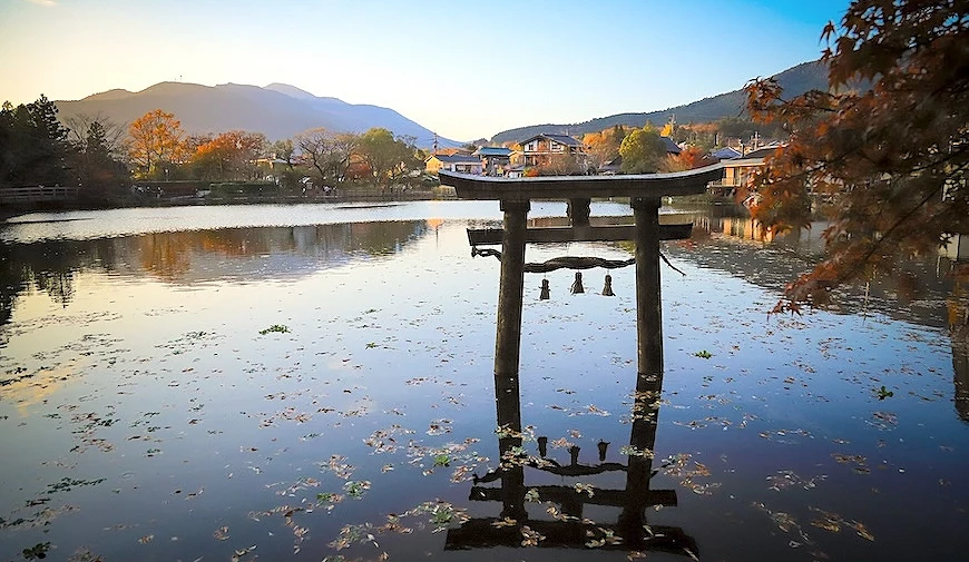 水中鳥居倒映於平靜湖面,背景為秋色樹木與遠山