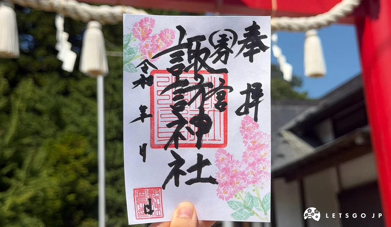 手中拿著寫有「國分一宮 諏訪神社」字樣並蓋有紅印、繪有粉色櫻花圖案的限定御朱印