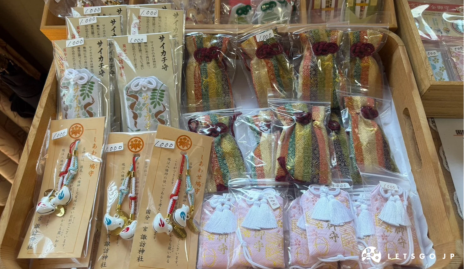 社務所木架上整齊陳列多款精美御守,包含繽紛彩帶造型的幸福御守與立體鴿子吊飾。