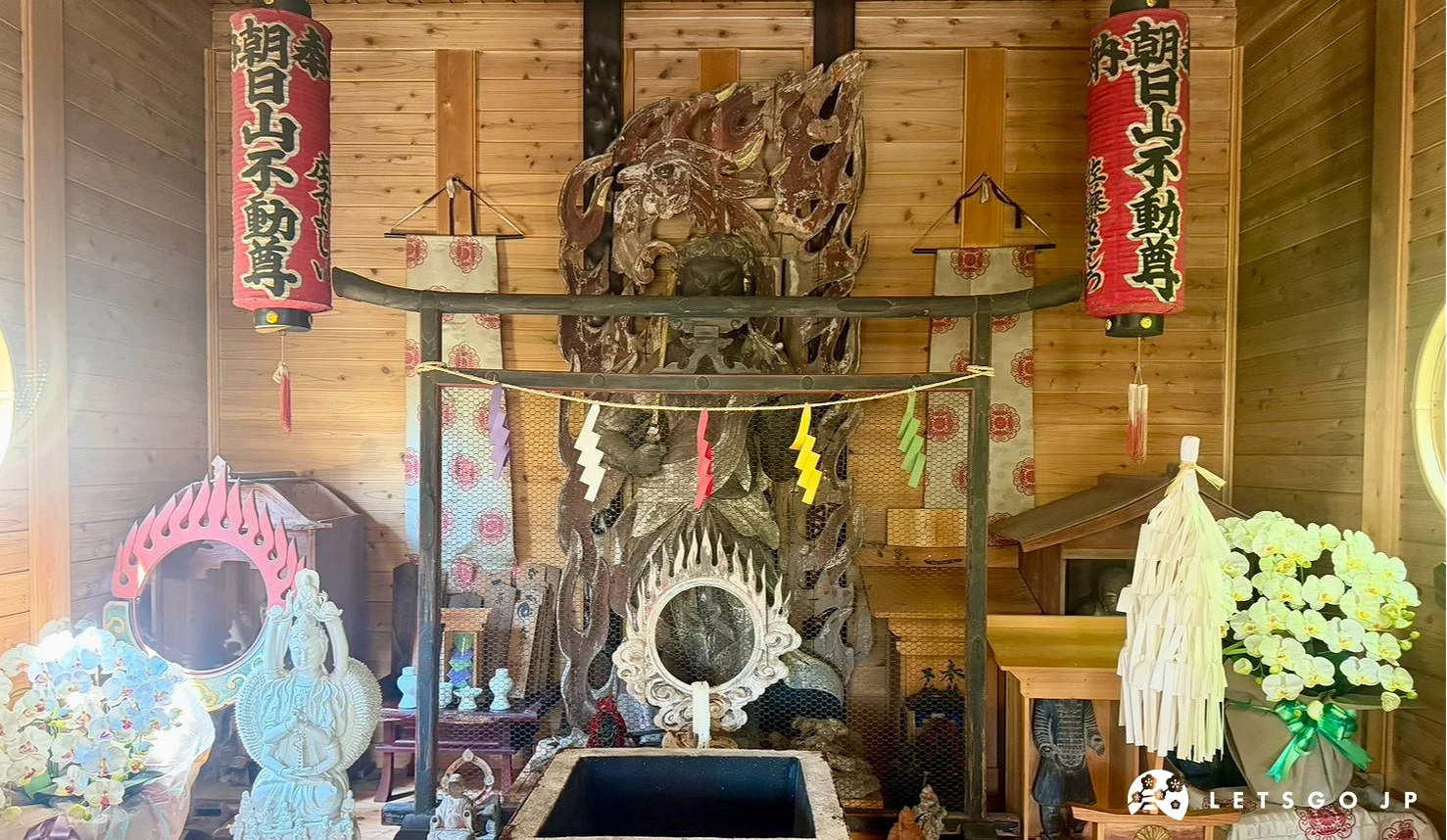 神殿內部的木造祭壇,中央設有圓形神鏡與祭祀神具,後方供奉著不動明王尊像,上方懸掛著寫有「朝日山不動明王」與「國分一宮諏訪神社」的紅底燈籠。