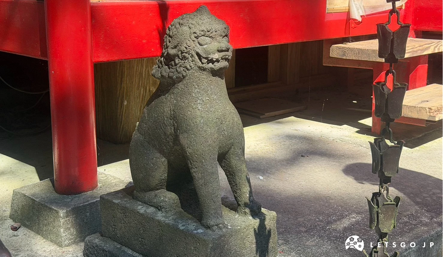 鎮守在社殿前方的石獅子(狛犬)雕像,石雕細節清晰,背景為鮮紅色的建築基座。