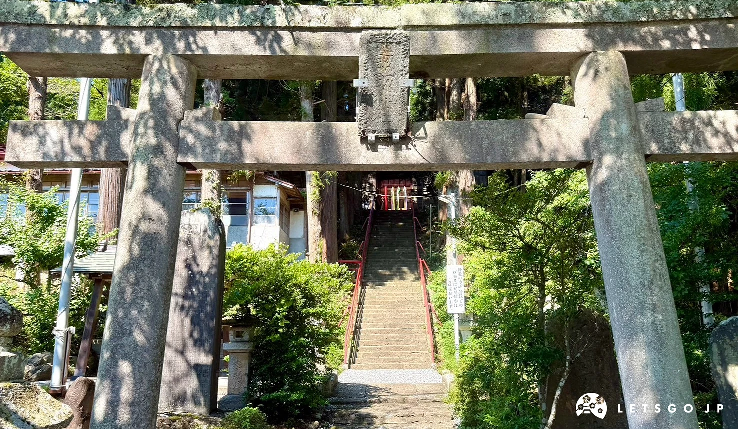 歷史悠久的灰色石造鳥居,穿過鳥居可看到後方的石階參道與茂密森林,氣氛古樸寧靜。