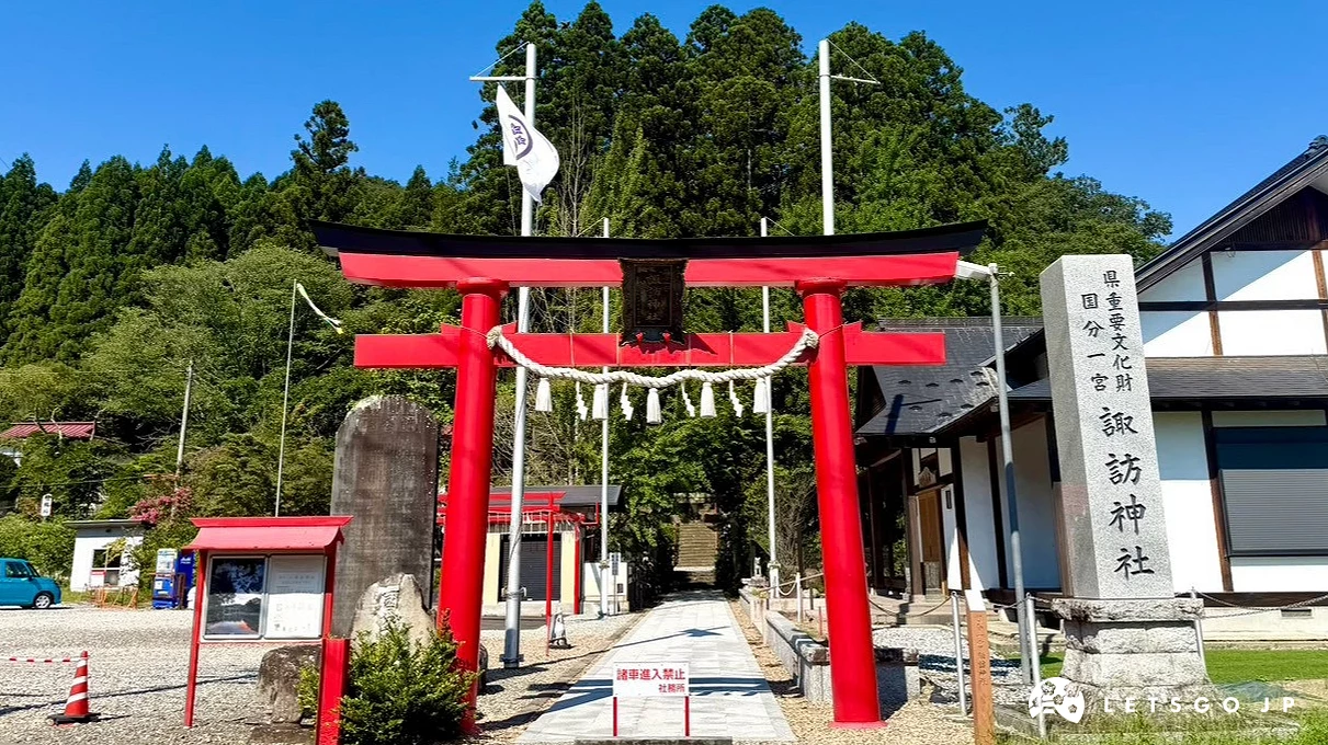 國分一宮諏訪神社入口處的鮮紅色大鳥居,鳥居下方掛有注連繩,後方延伸出平坦的參道與茂密的綠樹山林。