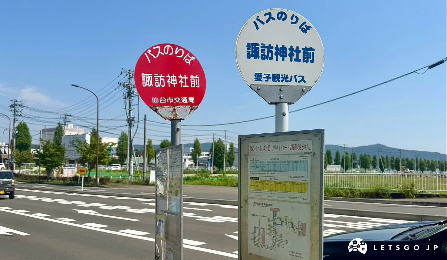 馬路旁設有兩座公車站牌,圓形標牌上寫著「諏訪神社前」,背景為寬廣的道路與晴朗天空。