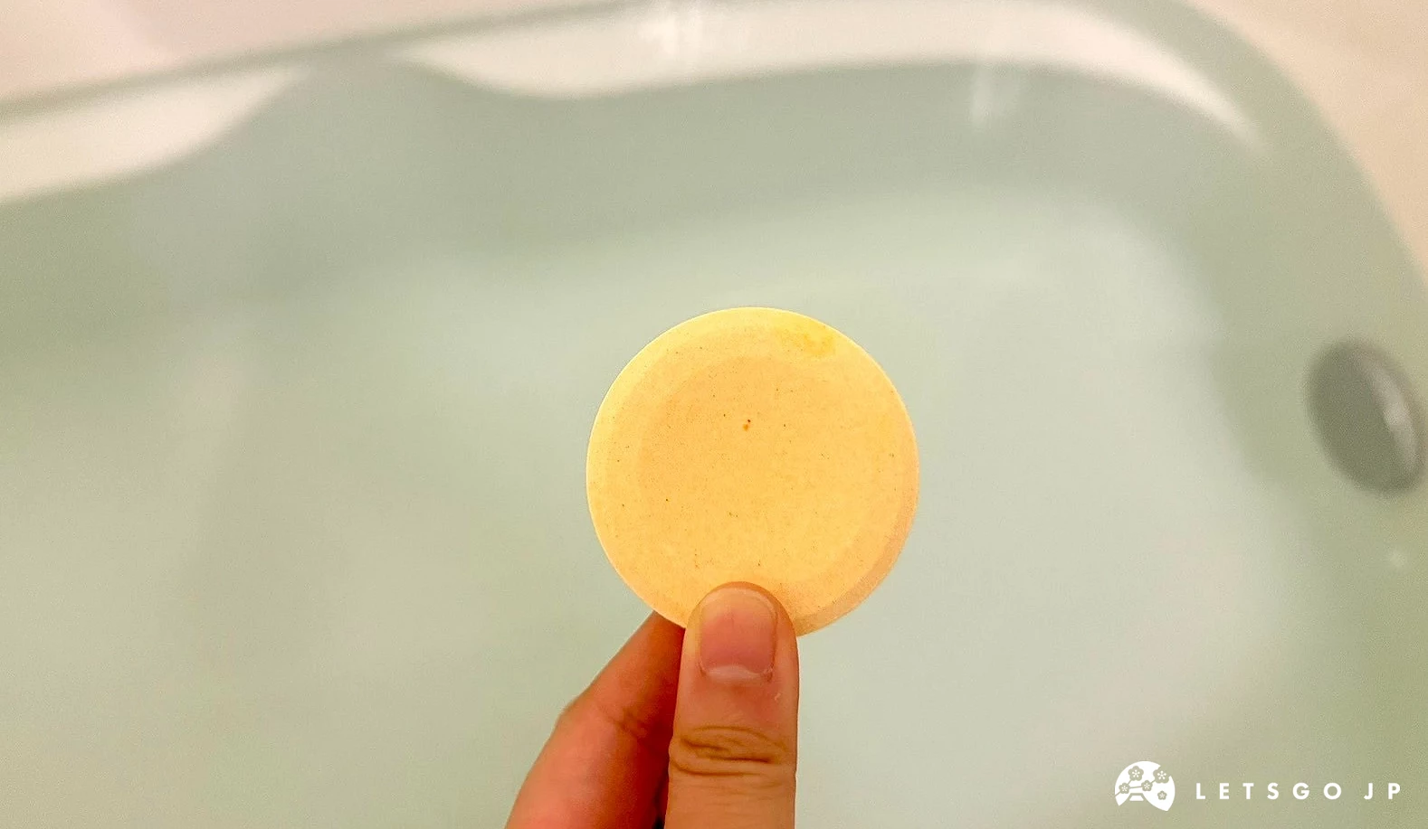 手持圓形黃色溫泡碳酸入浴錠於浴缸水面上的特寫