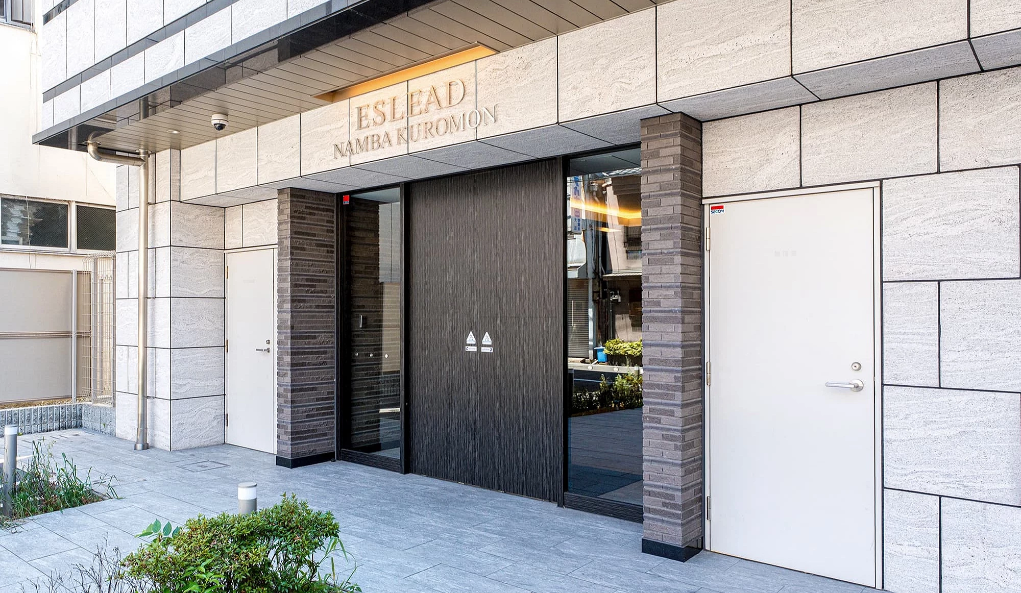 ESLEAD NAMBA KUROMON 建築入口外觀,設有深色自動門與石材外牆,前方有低矮綠化植栽