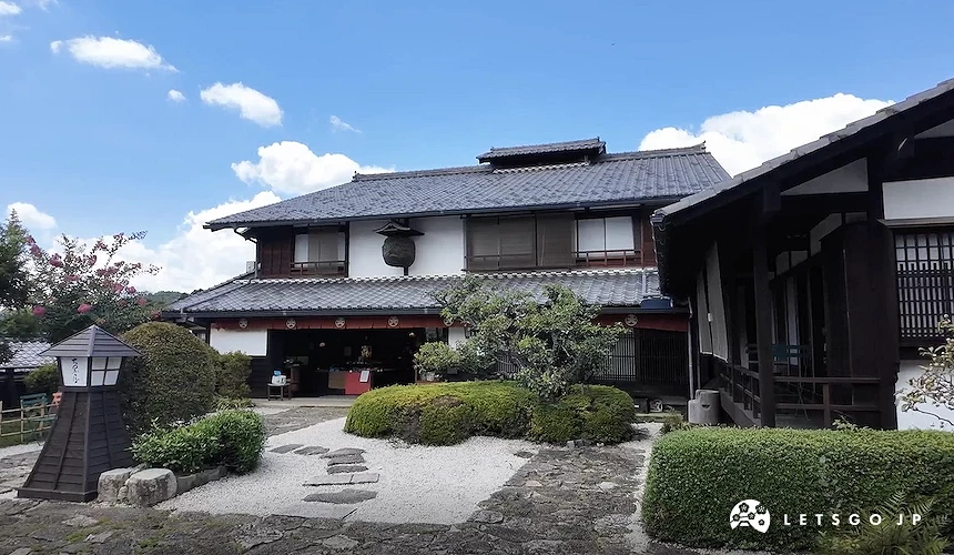 傳統日式兩層樓建築,前方設有枯山水庭園與修剪灌木,晴天藍空背景