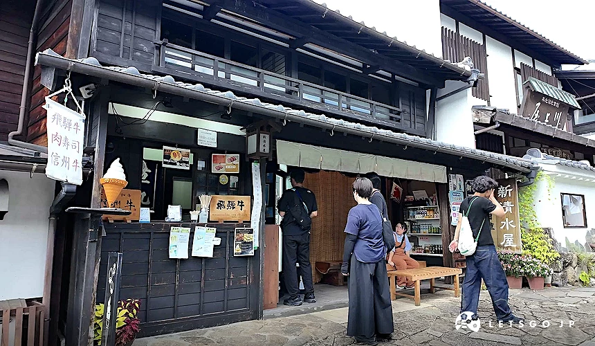 傳統日式商店街建築,店面掛有「飛驒牛・肉壽司・信州牛」招牌,數名顧客站立於店前