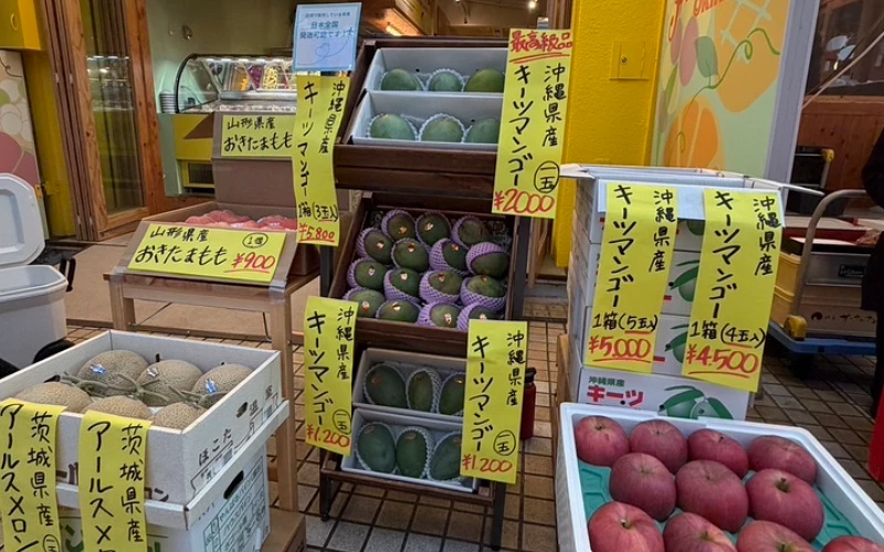 水果攤陳列沖繩產芒果、哈密瓜與蘋果,掛黃色手寫價格牌