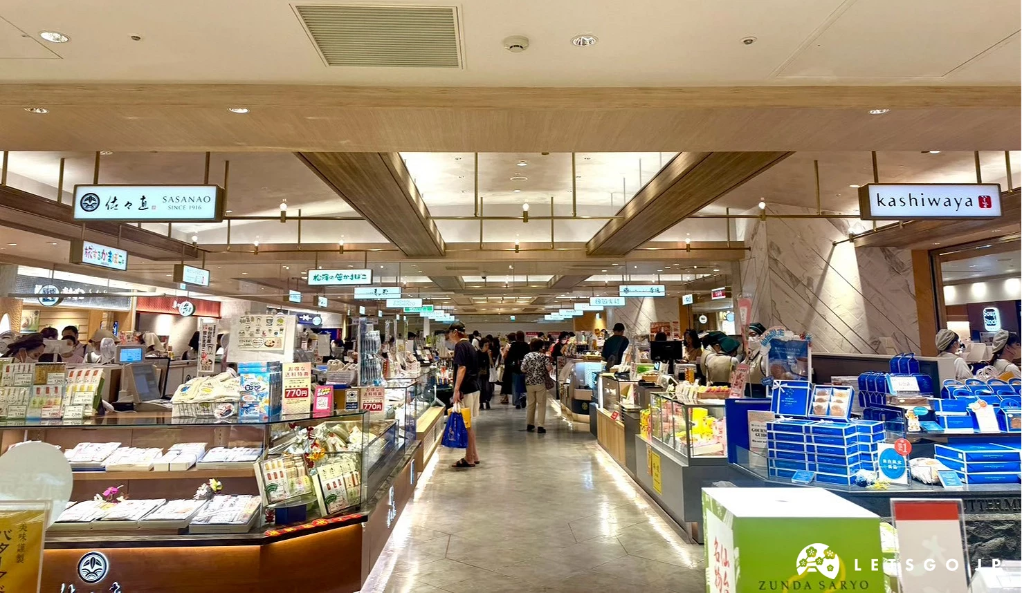 本館地下 1 樓乾淨明亮商場通道,兩側為各式伴手禮與專櫃攤位,頂部為木質格柵天花板。