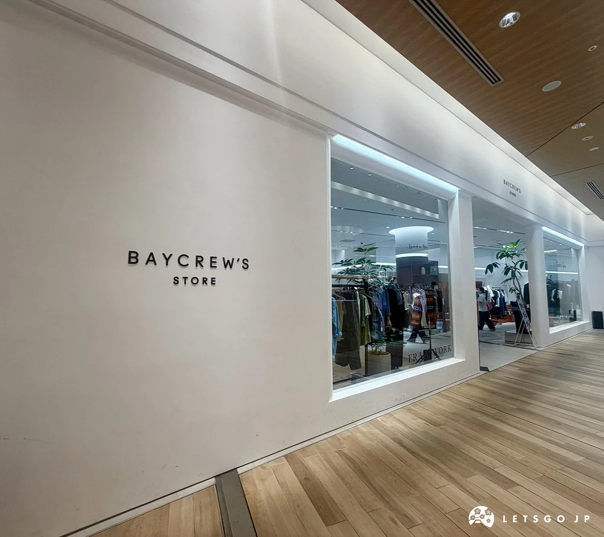 「BAYCREW'S STORE」簡約白色牆面與極簡風格品牌標誌,旁邊有寬敞的專櫃入口與服飾陳列。