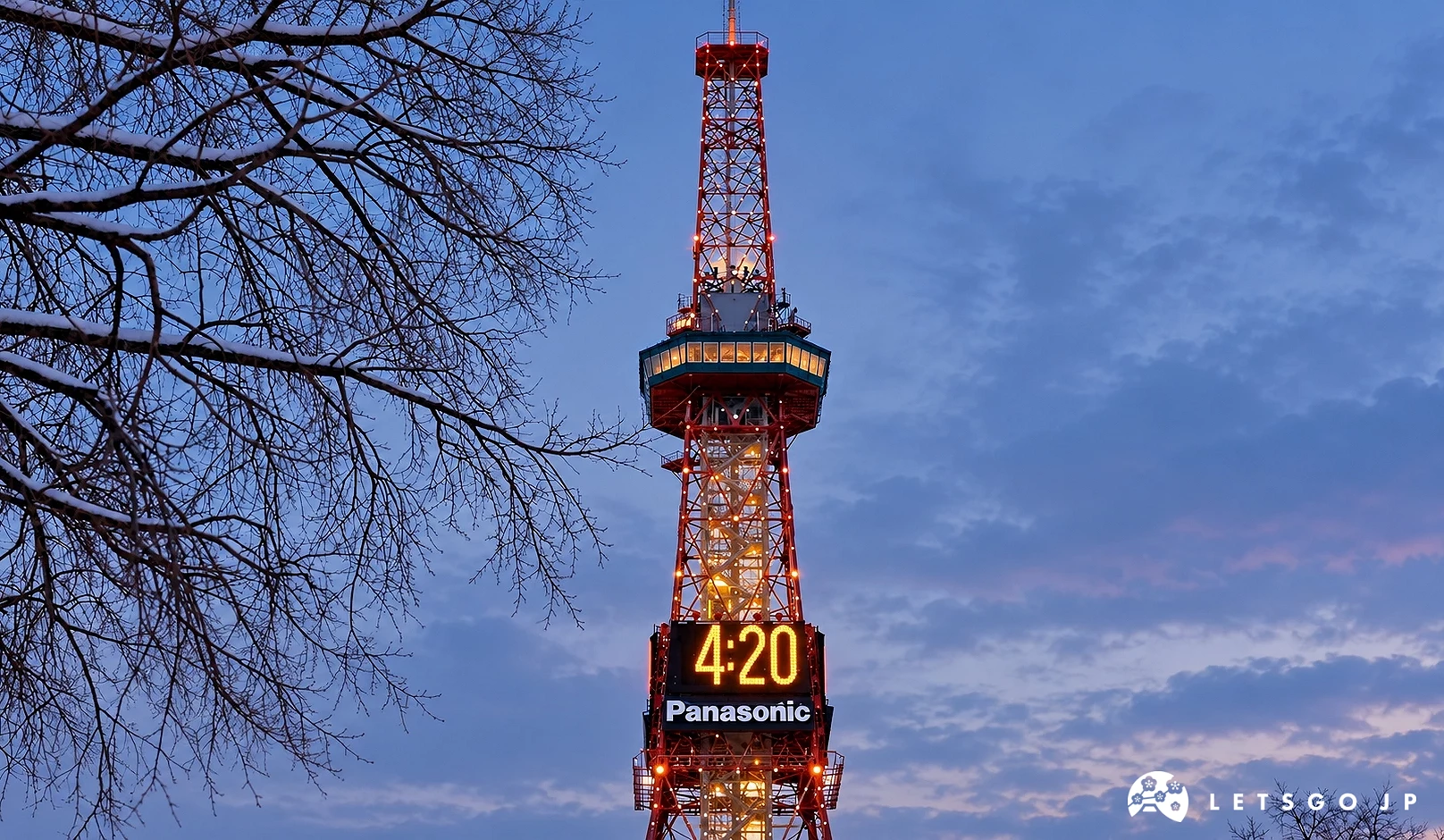 黃昏天空下的紅白色電視塔亮著燈,塔上「Panasonic」電子時鐘顯示4:20,左側有覆雪的樹枝