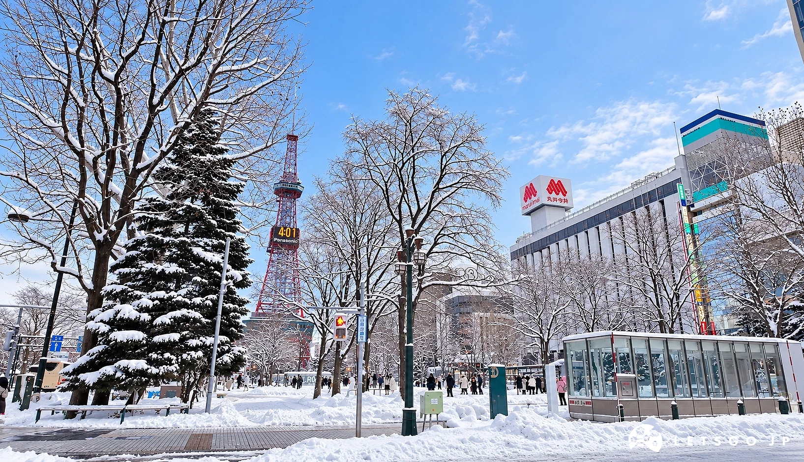 積雪的街道上有覆雪樹木與行人,遠處有紅白色電視塔,右側大樓掛有「丸井今井」招牌