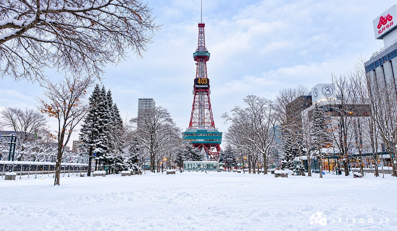 積雪的公園中央有紅白色電視塔,塔上有「Panasonic」電子時鐘,兩側有覆雪樹木,右側大樓掛有「丸井今井」招牌