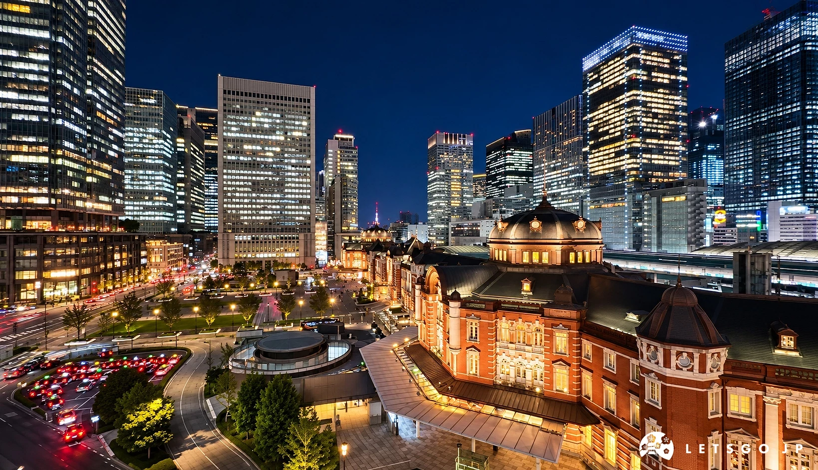 夜晚高樓大廈燈火通明,前方有紅磚造圓頂車站建築,左側道路上車輛亮著紅色車燈。