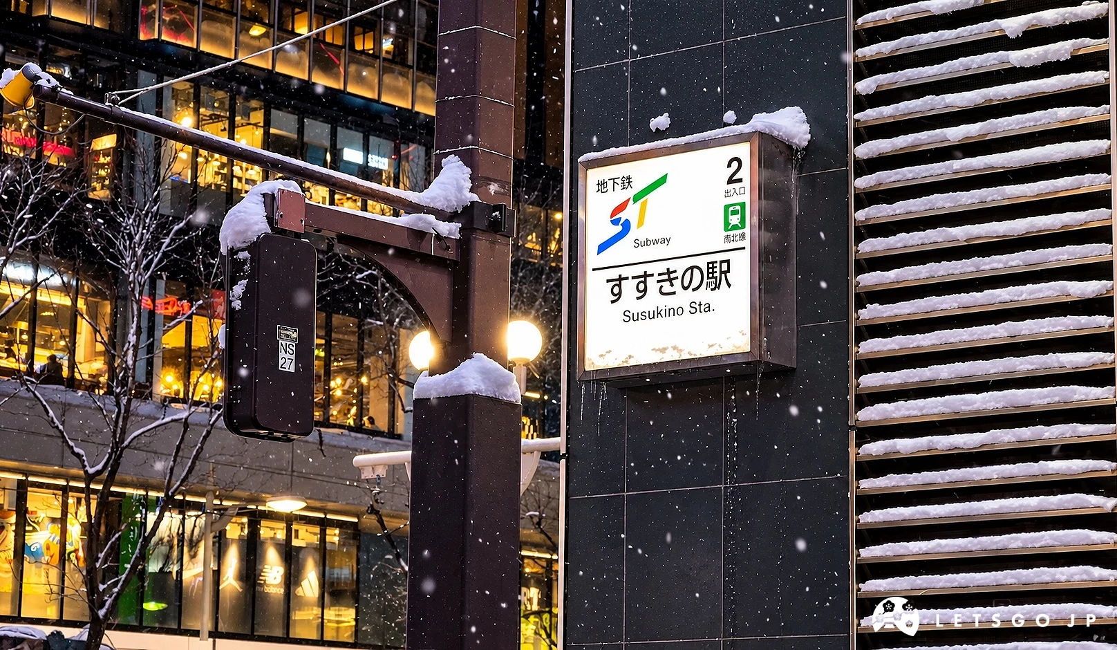 雪夜中地下鐵2號出入口的「すすきの駅」站牌覆有積雪,旁邊有路燈與百葉牆面