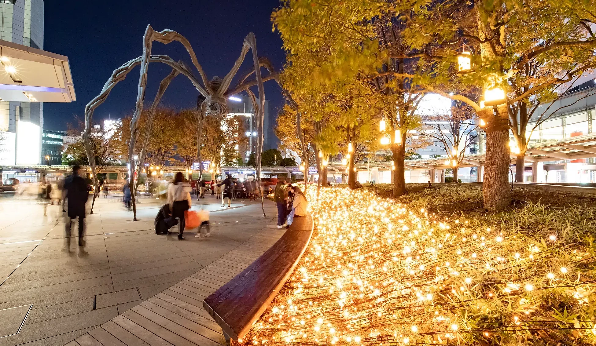 六本木之丘66廣場夜景,香檳金燈飾沿植栽鋪展,與大型蜘蛛雕塑同框