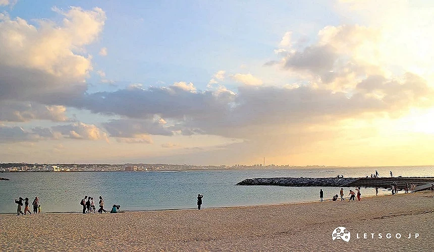 沖繩海灘夕陽景色,旅客漫步於沙灘與海堤。