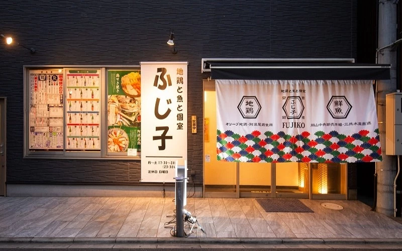 夜晚的店面外觀，門口掛有白色布簾，旁邊立有直式招牌，寫有店名「ふじ子」