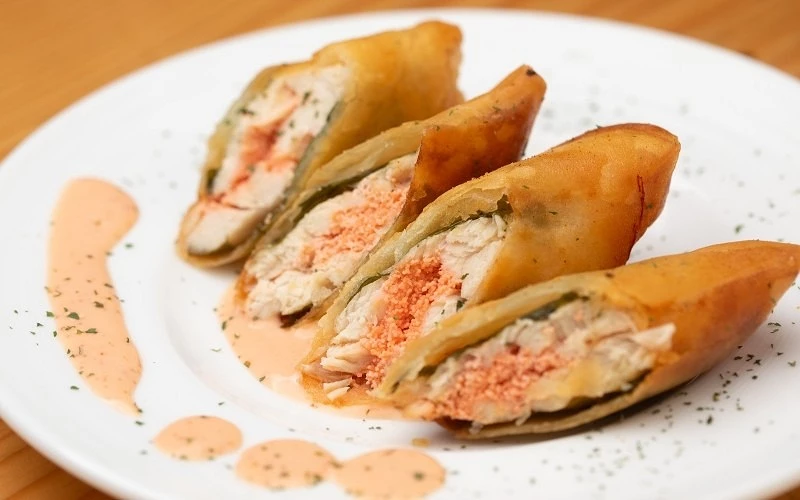 白盤上擺著切開的酥炸捲，內餡為雞肉與橘色餡料，旁邊淋有粉橘色醬汁