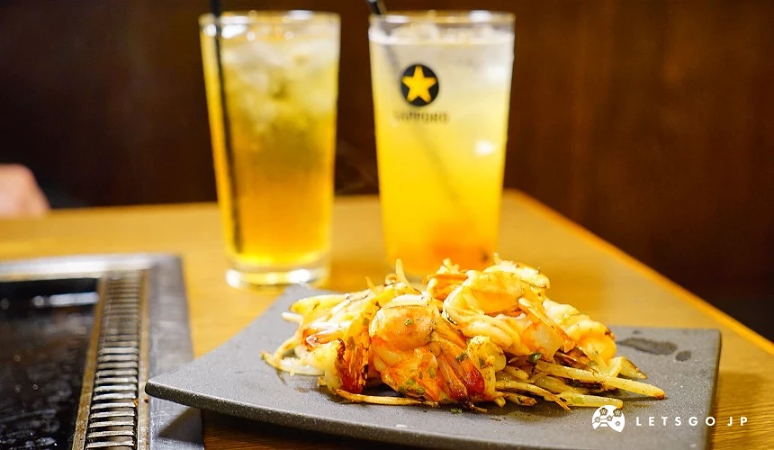 方形黑盤盛裝蝦與鐵板燒食材,後面有兩杯飲料