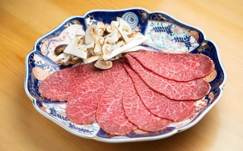 花紋圓盤中擺放扇形排列的霜降牛肉片與切片菇類