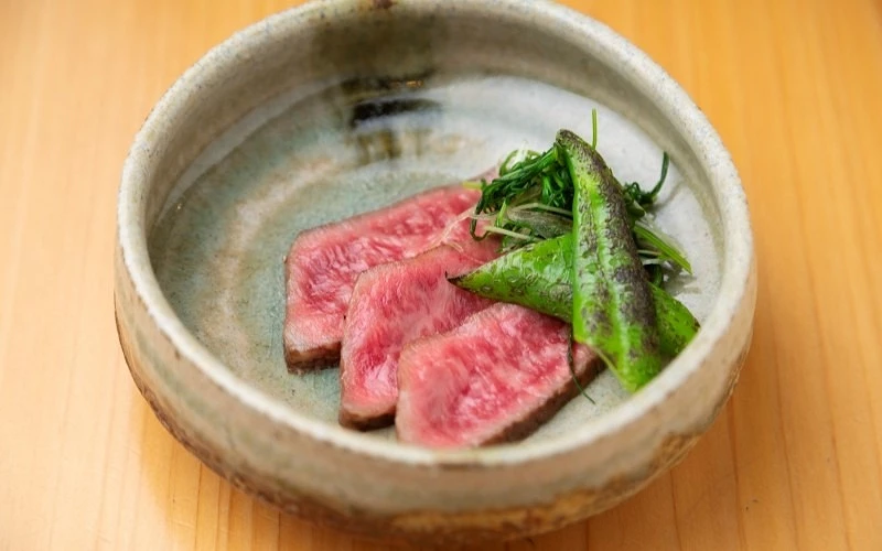 灰色陶碗中盛放三片切開的牛肉與青椒、青蔥絲