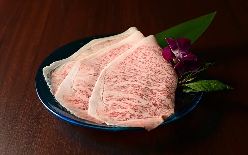藍色圓盤上擺放三片霜降牛肉片，旁有竹葉與紫色蘭花
