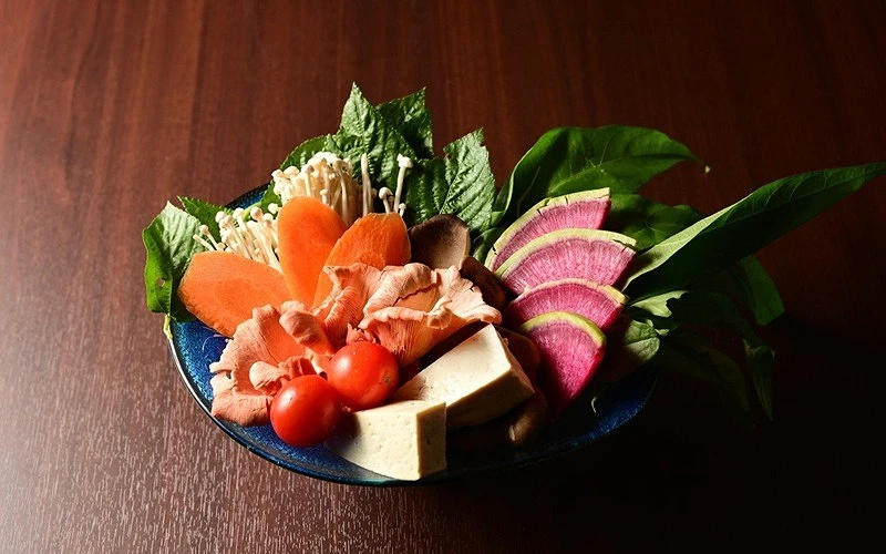 藍色碗中盛放紅蘿蔔、金針菇、蠔菇、小番茄、豆腐、西瓜蘿蔔與青菜