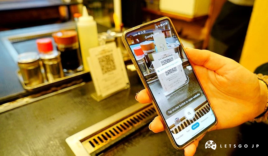 一隻手握持手機,對焦於放在桌面上的QRcode立牌