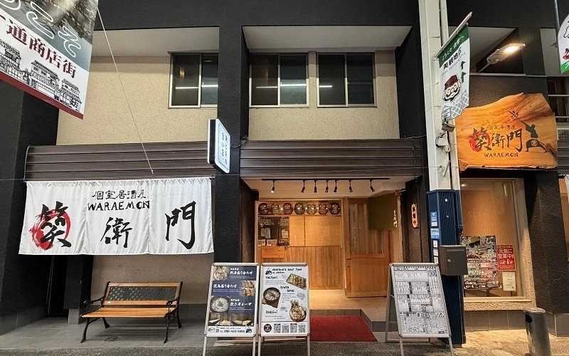 掛有「笑衛門 WARAEMON」布簾與木製招牌的居酒屋店面,門口擺放立牌與長椅