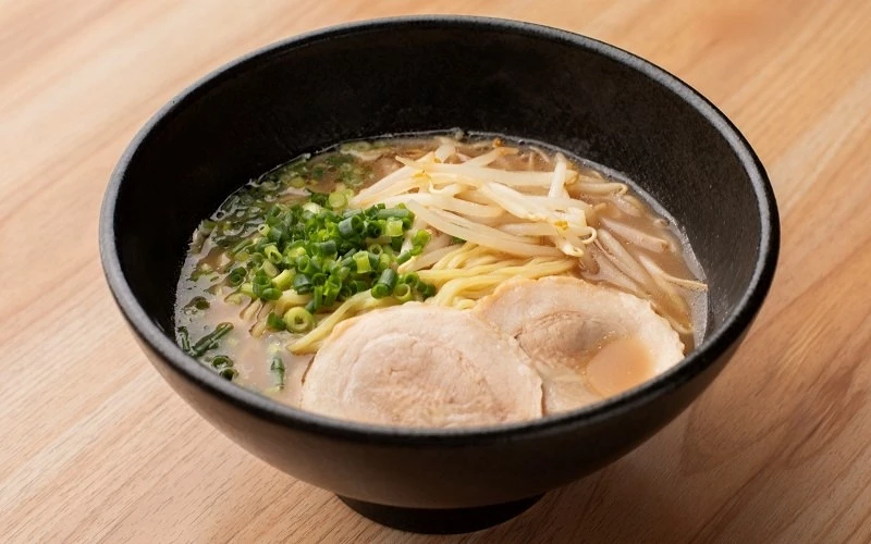 黑色碗中盛裝拉麵,配有叉燒、豆芽菜與蔥花