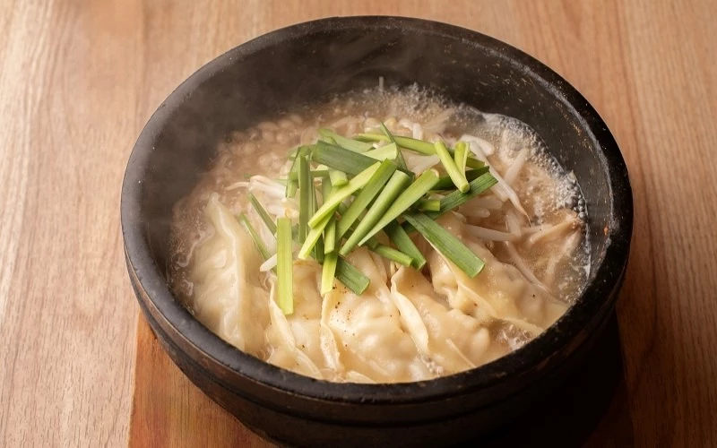 黑色石鍋中盛裝水餃與湯汁,上方鋪有韭菜