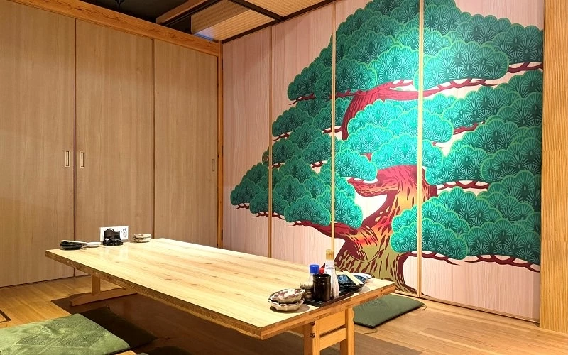 設有木質矮桌與坐墊的和室包廂,牆面繪有綠色松樹