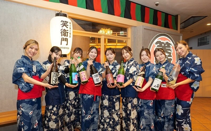 十位身穿藍色浴衣的店員手持日本酒瓶,背後有寫有「笑衛門」的白色燈籠