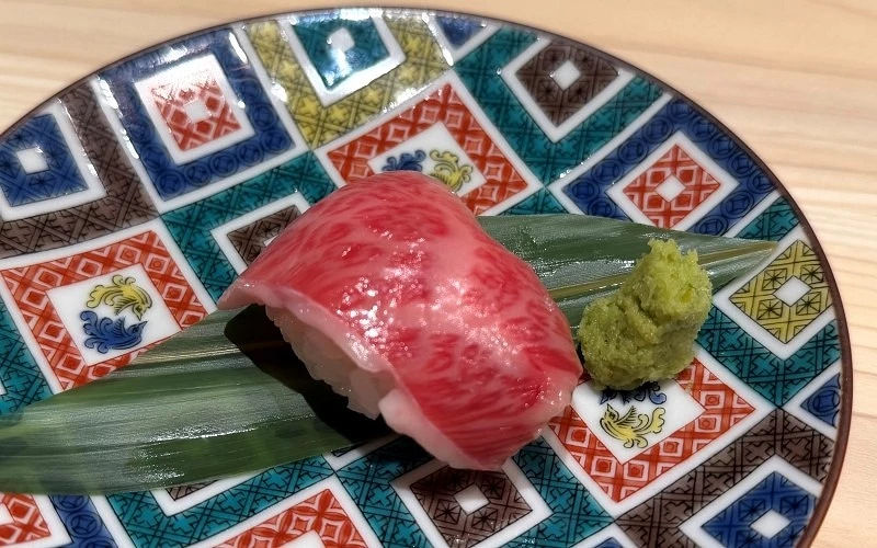 彩色幾何花紋盤中放有一貫牛肉握壽司,旁附山葵與竹葉