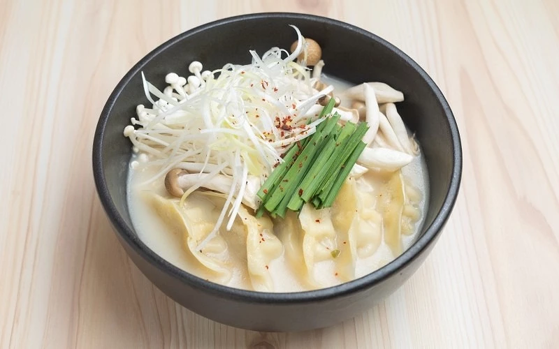 黑色碗中盛裝水餃與菇類,上方放有蔥絲與韭菜