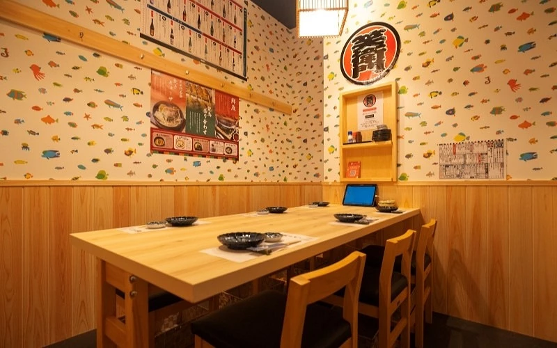 貼有魚類圖案壁紙的包廂座位區,木質長桌上放有平板與餐具