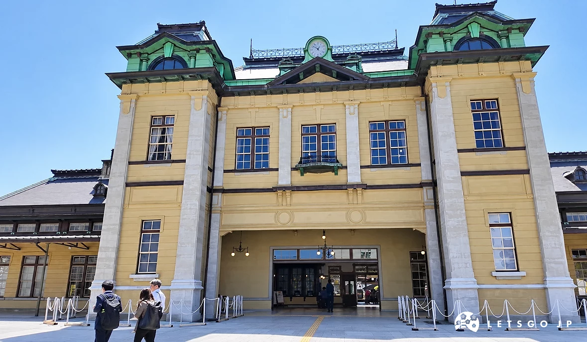門司港車站外觀,米白色洋風建築搭配綠色屋頂,中央設有時鐘,前方為廣場與遊客