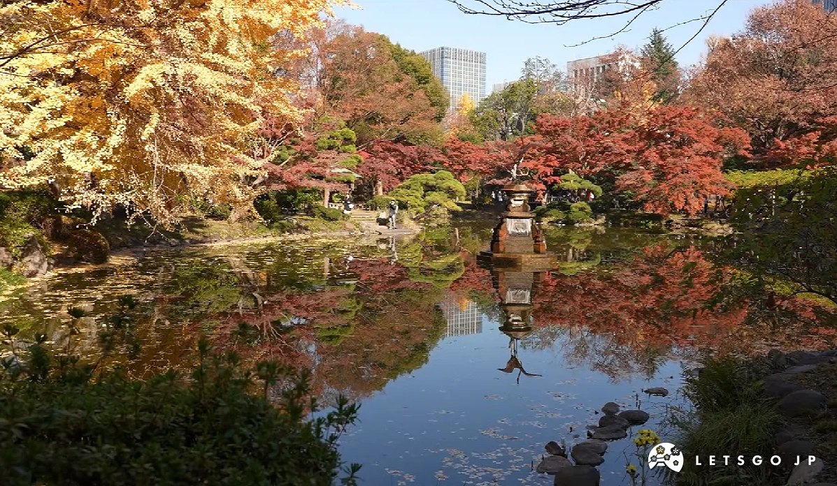 東京日比谷公園噴水池塘畔紅葉與黃葉交織,遠方高樓林立"