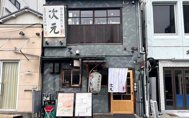 灰色外牆的店面，招牌寫有「次元」，門口掛有白色暖簾與燈籠