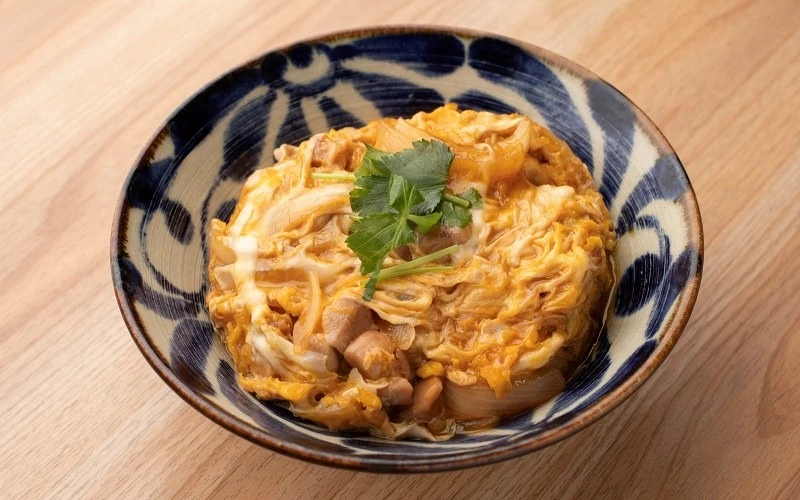 藍白花紋碗中盛裝蛋液雞肉丼飯，上方放有三葉芹