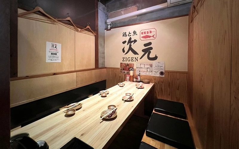 牆面寫有「次元 ZIGEN」的木質長桌座位區，桌上擺放餐具與坐墊
