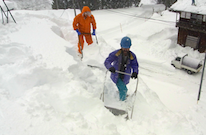 兩個人在積雪很厚的房子前除雪